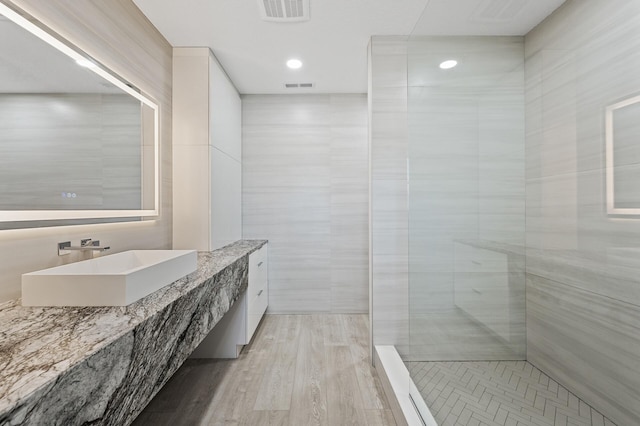 full bathroom featuring tiled shower, tile walls, visible vents, and a sink
