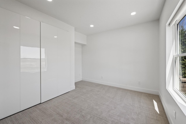 unfurnished bedroom featuring recessed lighting, baseboards, light colored carpet, and a closet