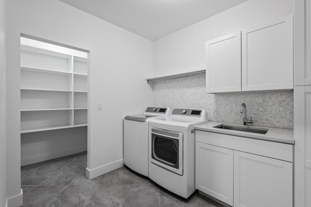 laundry area with cabinet space, a sink, dark tile patterned flooring, baseboards, and separate washer and dryer