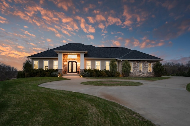 view of front of property featuring curved driveway, french doors, a front yard, and stone siding