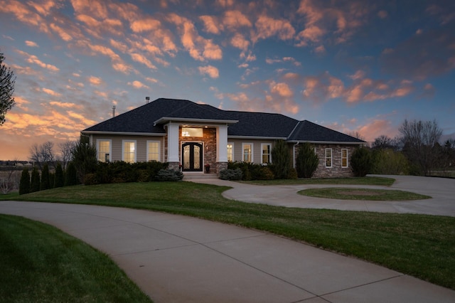 view of front of home featuring curved driveway, a lawn, french doors, and stone siding