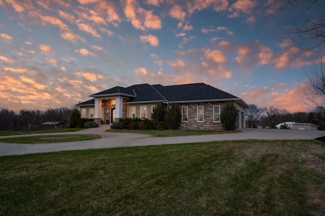view of front of house featuring curved driveway, an attached garage, a yard, and stone siding