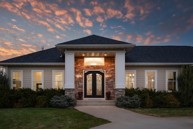 doorway to property with a lawn, roof with shingles, and stone siding
