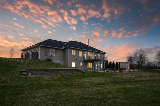 back of property at dusk featuring a garage, a wooden deck, a lawn, and a patio area
