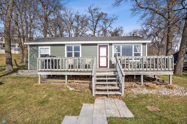view of front of house with a deck, a chimney, a shingled roof, and a front yard