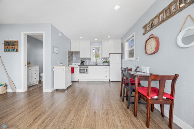 kitchen featuring wood finished floors, white appliances, baseboards, white cabinets, and tasteful backsplash