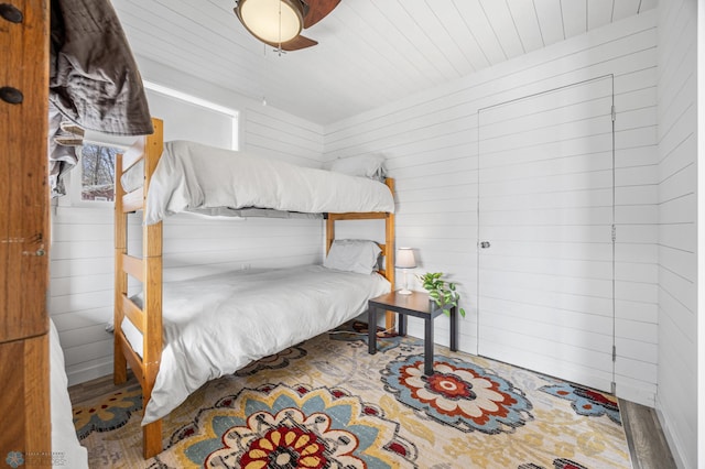 bedroom featuring wooden ceiling, a ceiling fan, wood walls, and wood finished floors