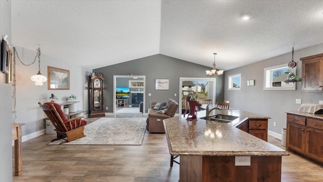 kitchen with light wood-style floors, an island with sink, a textured ceiling, a sink, and vaulted ceiling