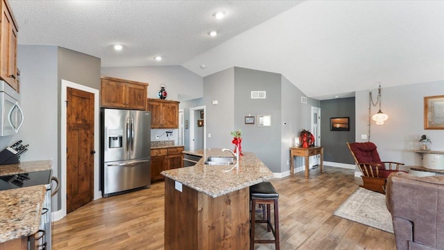 kitchen featuring appliances with stainless steel finishes, vaulted ceiling, brown cabinets, a sink, and a breakfast bar