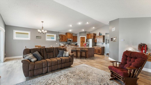 living room featuring baseboards, an inviting chandelier, lofted ceiling, and light wood-style floors