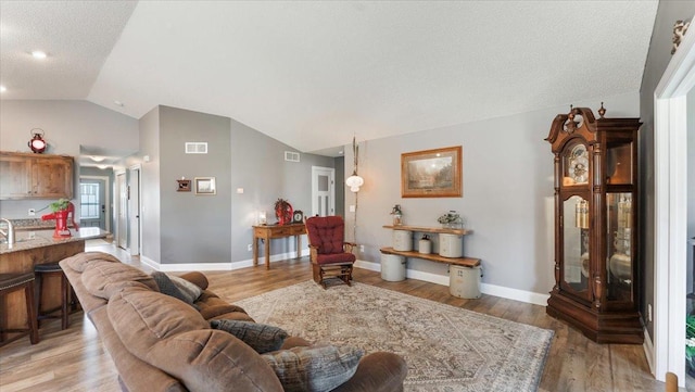 living room featuring light wood-style floors, baseboards, visible vents, and lofted ceiling