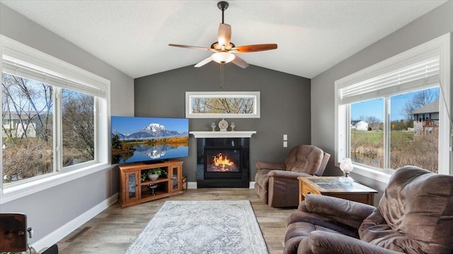 living room with a glass covered fireplace, light wood-style floors, baseboards, ceiling fan, and vaulted ceiling