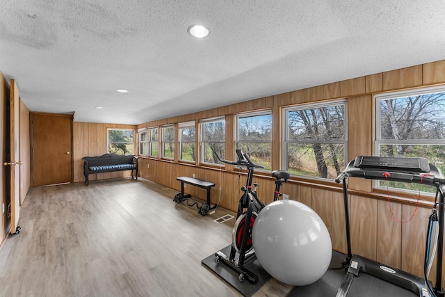 exercise area with a textured ceiling, wood walls, light wood-style flooring, and visible vents