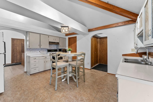 kitchen with a sink, arched walkways, beamed ceiling, and light countertops