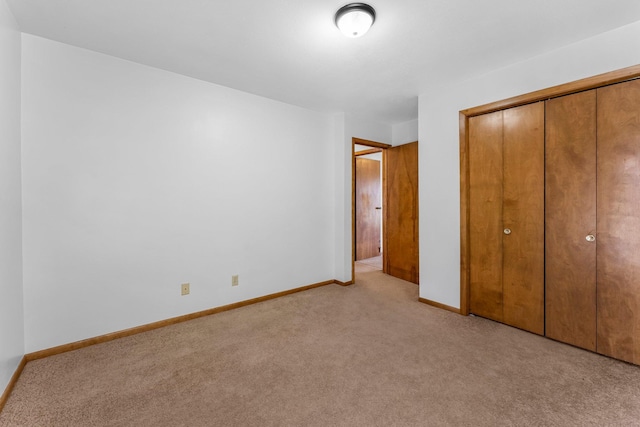unfurnished bedroom featuring baseboards, light carpet, and a closet
