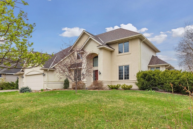 traditional-style home featuring an attached garage, a front lawn, roof with shingles, and stucco siding