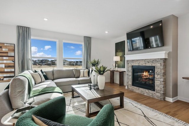 living area featuring light wood-style floors, baseboards, recessed lighting, and a stone fireplace