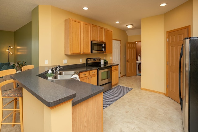 kitchen featuring a sink, a breakfast bar, dark countertops, stainless steel appliances, and a peninsula