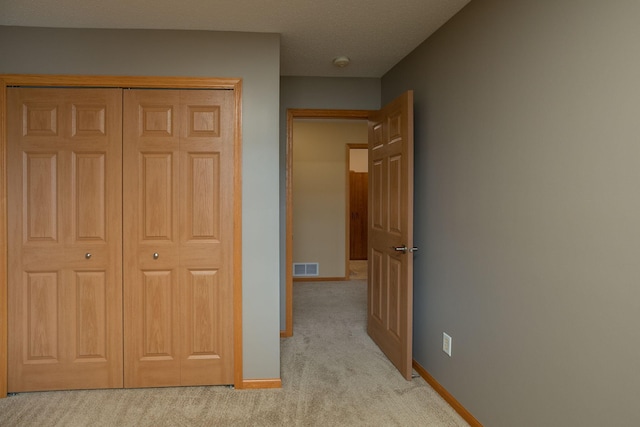 hall with visible vents, light colored carpet, and baseboards