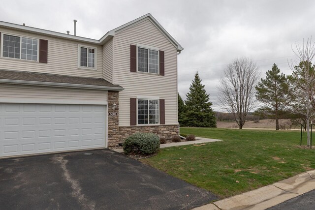 traditional-style home with an attached garage, aphalt driveway, a front lawn, and stone siding