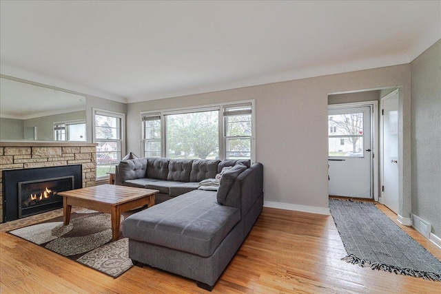living area featuring baseboards, light wood finished floors, a stone fireplace, and a wealth of natural light