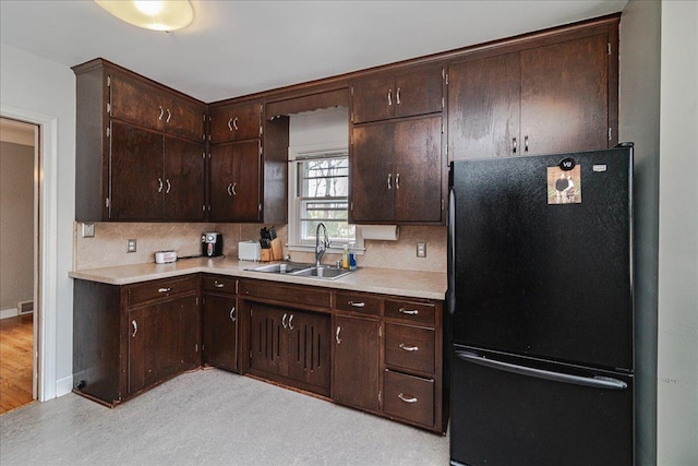 kitchen with a sink, light countertops, freestanding refrigerator, and dark brown cabinets
