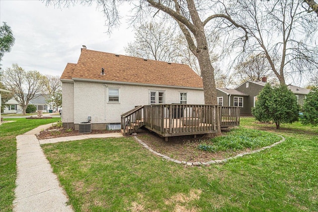 back of house featuring roof with shingles, a wooden deck, stucco siding, central AC unit, and a lawn
