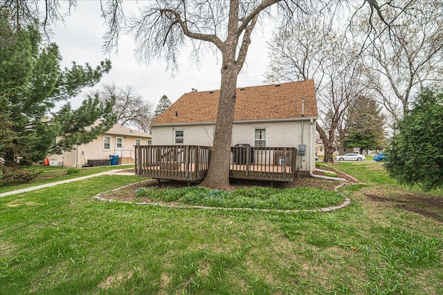 back of property featuring stucco siding, roof with shingles, a wooden deck, and a yard