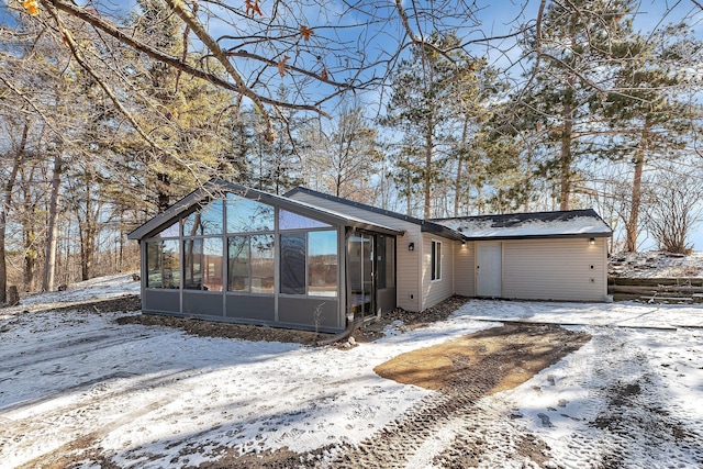 snow covered rear of property featuring a sunroom