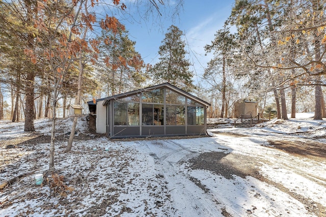 snow covered back of property featuring a sunroom