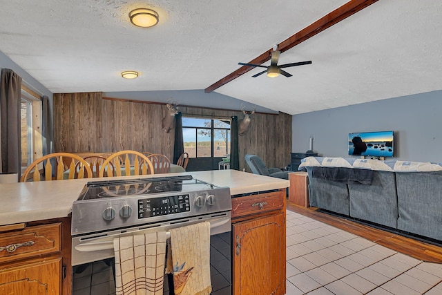kitchen featuring lofted ceiling with beams, electric range, a ceiling fan, wood walls, and light countertops