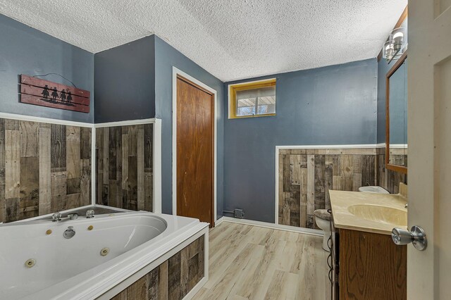 bathroom featuring wood finished floors, vanity, a textured ceiling, and a tub with jets