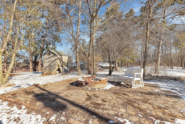 snowy yard featuring an outbuilding, an outdoor fire pit, and a storage unit