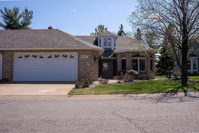 view of front of home with a front lawn, concrete driveway, brick siding, a garage, and a shingled roof
