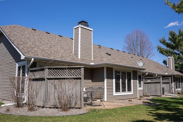 back of house featuring a yard, a patio area, a shingled roof, and a chimney
