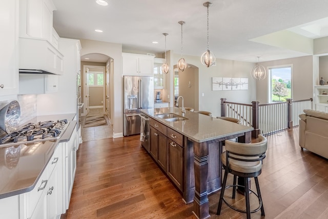 11328 Blazingstar Ln, Lake Elmo, MN 55042 - kitchen featuring a sink, stainless steel appliances, a breakfast bar area, arched walkways, and dark wood-type flooring