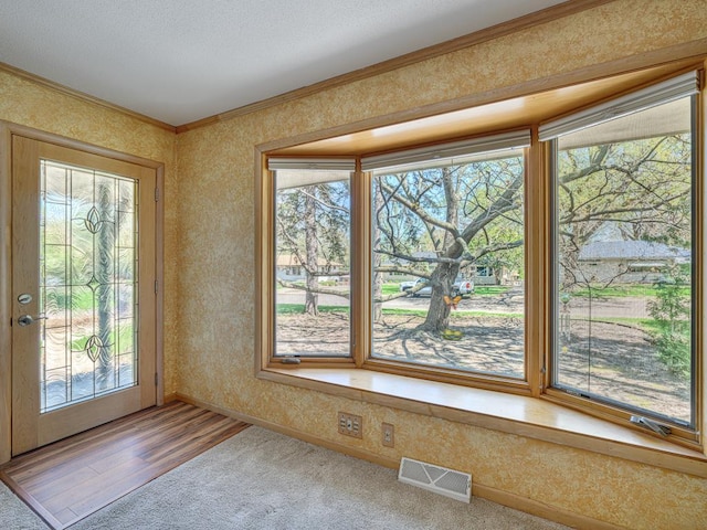 doorway to outside featuring crown molding, plenty of natural light, visible vents, and wallpapered walls