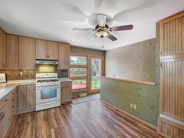 kitchen featuring wood finished floors, under cabinet range hood, decorative backsplash, light countertops, and white range with gas stovetop