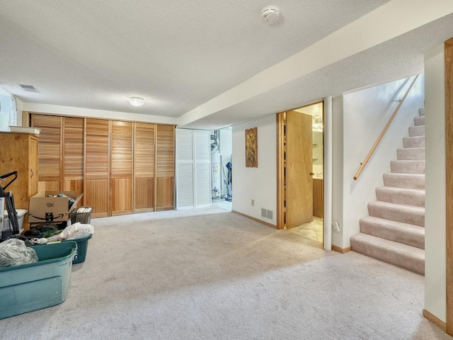 basement featuring light colored carpet, stairs, a textured ceiling, and visible vents