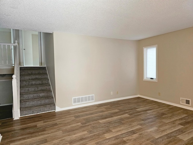 unfurnished room with a textured ceiling, wood finished floors, visible vents, and stairs