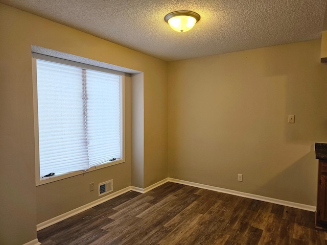 unfurnished room featuring baseboards, visible vents, a textured ceiling, and dark wood finished floors