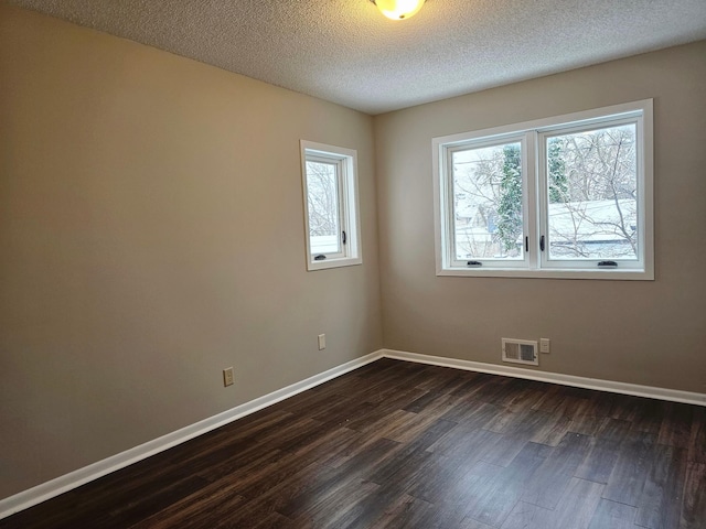 unfurnished room featuring a textured ceiling, dark wood finished floors, visible vents, and baseboards