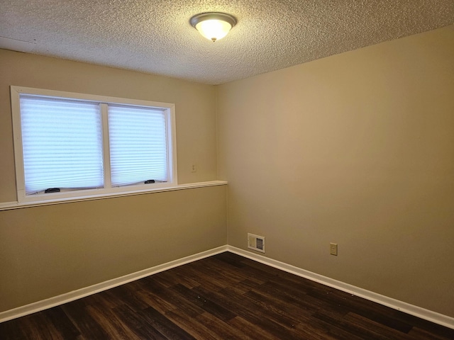 spare room with baseboards, dark wood-style flooring, a textured ceiling, and visible vents