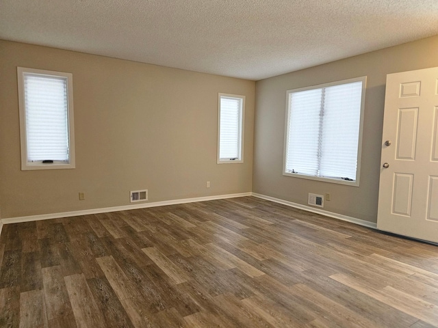 empty room featuring baseboards, dark wood-style flooring, a textured ceiling, and visible vents