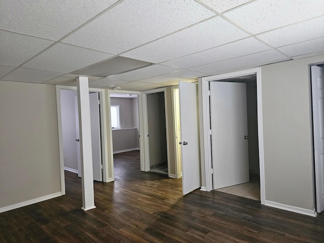 basement with dark wood finished floors, baseboards, and a paneled ceiling