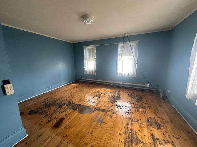 unfurnished room with a baseboard radiator, hardwood / wood-style floors, baseboards, and ornamental molding