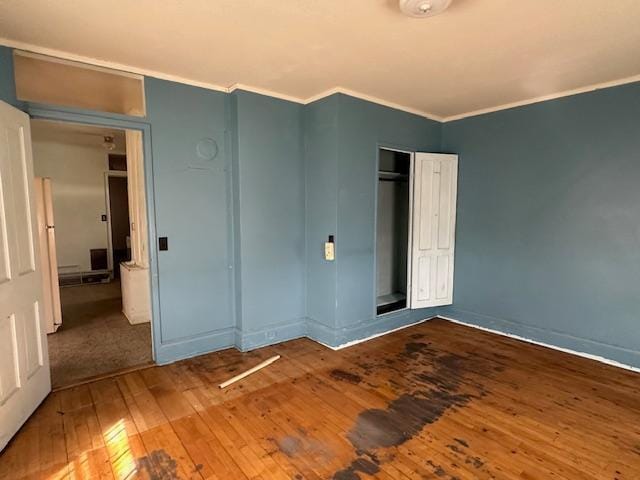unfurnished bedroom with crown molding, a closet, wood-type flooring, baseboards, and freestanding refrigerator