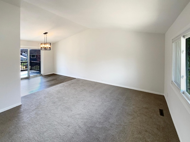 empty room featuring vaulted ceiling, dark carpet, a notable chandelier, and a healthy amount of sunlight