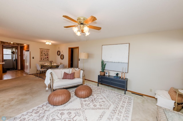 living room with ceiling fan, baseboards, and light colored carpet
