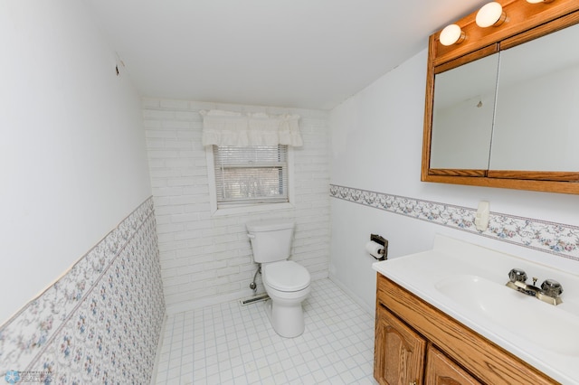 bathroom with tile patterned flooring, toilet, vanity, tile walls, and wainscoting